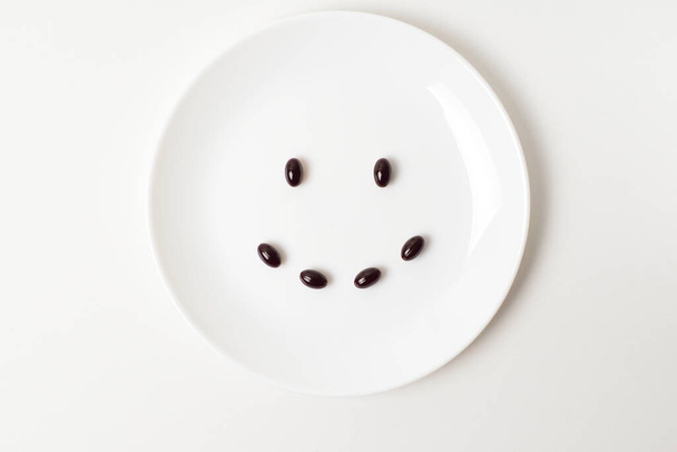 Lächeln aus dunklen Astaxanthin-Kapseln auf einem Teller. - Foto, Bild