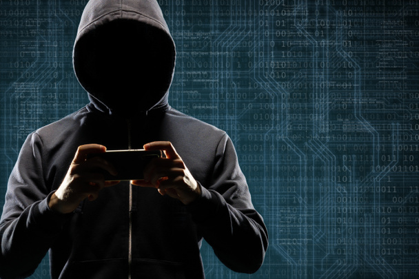 バイナリ コードとデジタル背景にスマート フォン ・ ガジェットを持つ危険なハッカー。マスクとフードに隠された暗い顔。データ泥棒、インターネット攻撃、ダークネット詐欺、仮想現実とサイバー セキュリティ - 写真・画像