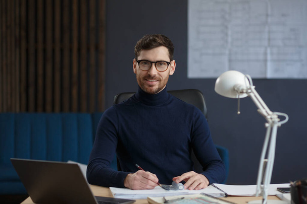 Architect working in office with blueprints.Engineer inspect architectural plan, sketching a construction project.Portrait of handsome bearded man sitting at workplace. Business construction concept - Fotó, kép