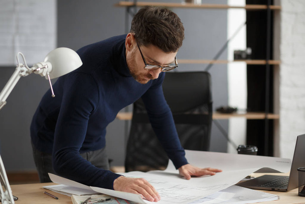 Architect working in office with blueprints.Engineer inspect architectural plan, sketching a construction project.Portrait of handsome bearded man sitting at workplace. Business construction concept - Foto, immagini
