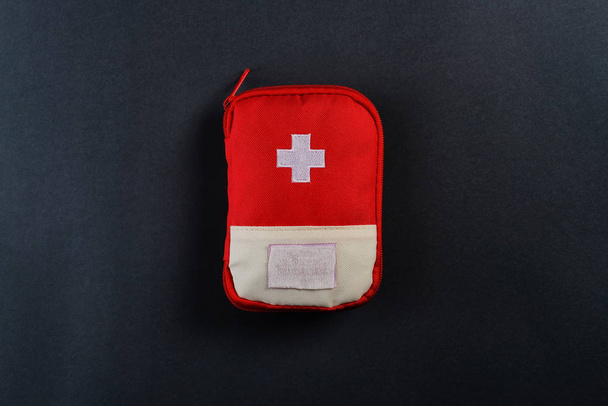 Закрытая красная сумка с аптечкой на тёмном фоне. Фото с копировальным пространством
 - Фото, изображение