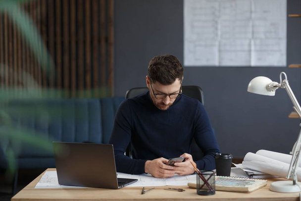 Architect working in office with blueprints.Engineer inspect architectural plan, sketching a construction project.Portrait of handsome bearded man sitting at workplace. Business construction concept - Foto, Bild