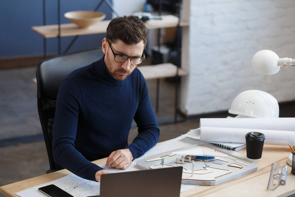 Architect working in office with blueprints.Engineer inspect architectural plan, sketching a construction project.Portrait of handsome bearded man sitting at workplace. Business construction concept - Foto, Imagen