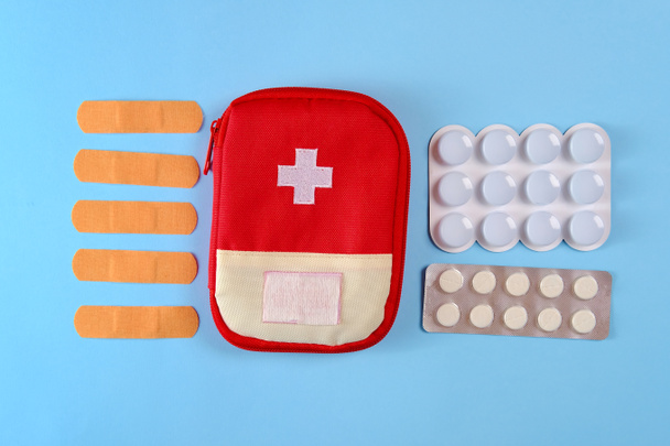Closed tourist first aid kit pouch near to the pills, adhesive bandages and nasal spray on the bright blue background - Fotoğraf, Görsel