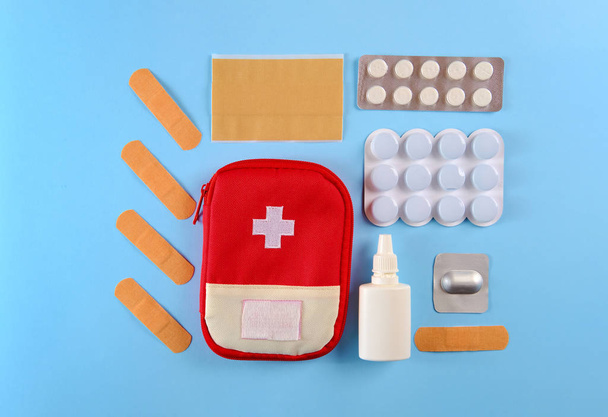 Closed tourist first aid kit pouch near to the pills, adhesive bandages and nasal spray on the bright blue background - Valokuva, kuva