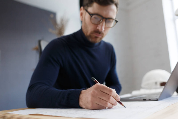 Architect working in office with blueprints.Engineer inspect architectural plan, sketching a construction project.Portrait of handsome bearded man sitting at workplace. Business construction concept - Foto, Imagem