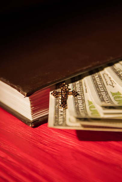 Zamknij pieniądze w księdze Biblii i mały złoty krzyż. - Zdjęcie, obraz