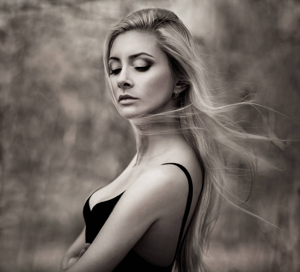 Portrait of young beautiful blonde woman in black top standing and looking down with blooming trees at background - Foto, Imagem