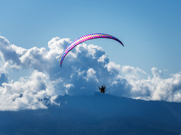 Άνθρωπος σε ένα αλεξίπτωτο πλαγιάς πάνω από τα βουνά με φόντο τα σύννεφα και τον γαλάζιο ουρανό - Φωτογραφία, εικόνα