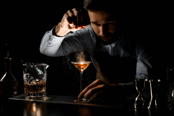 Cantinero rociando la bebida alcohólica en un vaso de martini con jugo de ralladura de orage
 - Foto, imagen