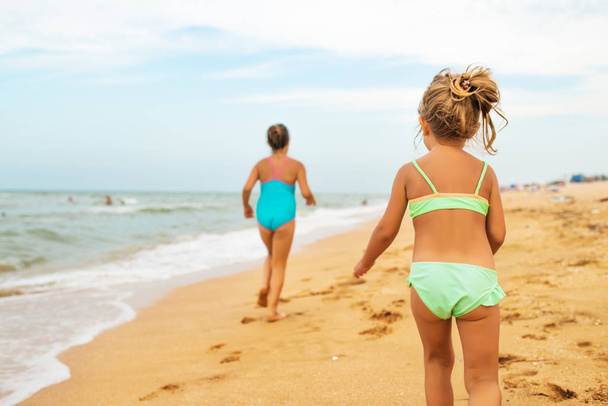 Two positive little girls run along sandy beach - Foto, Imagen