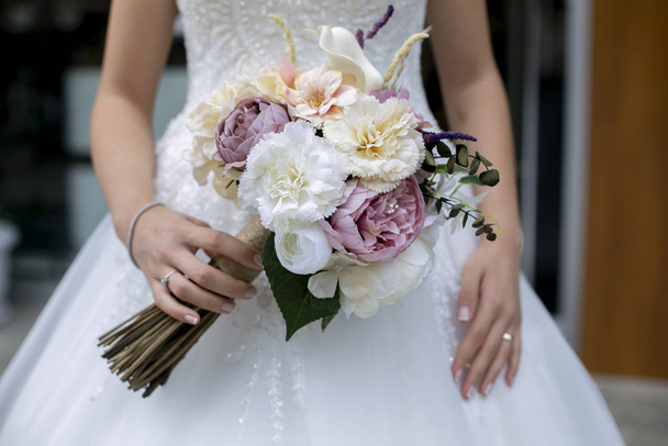 de bruid in de witte jurk en een bos bloemen in haar hand - Foto, afbeelding
