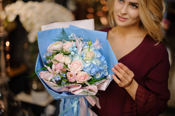Fille tenant un bouquet de printemps d'hortensias bleus et de roses crémeuses enveloppées dans du papier avec des feuilles vertes
 - Photo, image