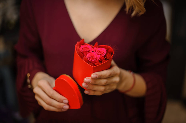 Girl holding a little heart shape box full of red feathers and pink roses - Фото, изображение