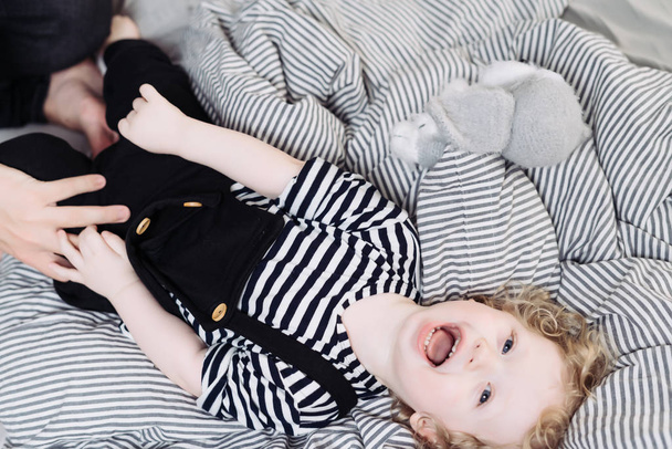 curly angel baby laughs lying on the bed, hands put on his pants - Fotoğraf, Görsel