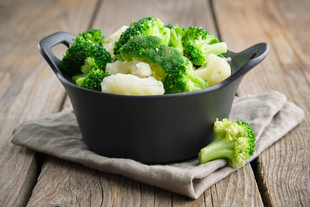 Black saucepan with cooked broccoli and cauliflower on wooden table. - Fotó, kép