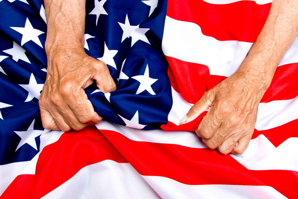 Elderly man hands compresses a USA flag. The concept of caring f - Zdjęcie, obraz