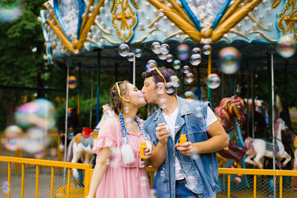 Egy gyönyörű, vidám, romantikus szerelmespár élvezi a szappanbuborékokat egy vidámparkban és csókolózik. - Fotó, kép