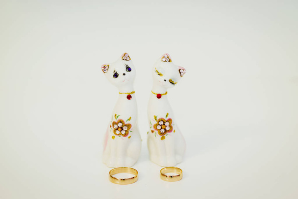 Anillos de boda dorados junto a un par de gatos de porcelana sobre fondo azul
 - Foto, Imagen