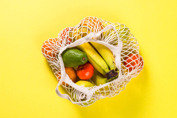Mesh bag with fruits on color background. - Fotografie, Obrázek