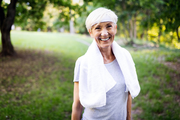 Portrait of smiling sporty senior woman with towel in park - Valokuva, kuva