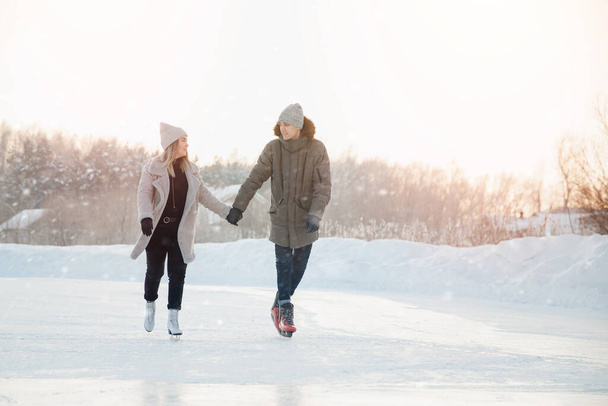 Dziewczyna i mężczyzna trzymają się za ręce patrząc na siebie i jedząc na mrożonym lodzie jeziora na łyżwach. W tle jest zachód słońca. - Zdjęcie, obraz