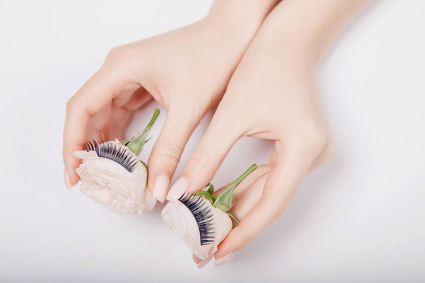 False eye lashes extension with hand woman white flowers on background. Concept beauty fashion - Photo, Image