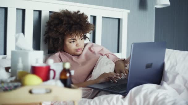 Sick freelancer african american girl with flu working in bed with notebook - Imágenes, Vídeo