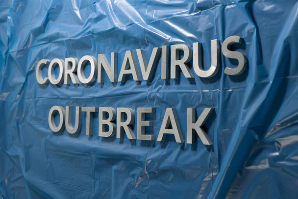 Las palabras brote de coronavirus colocadas con letras de metal plateado en una película plástica azul arrugada
 - Foto, imagen