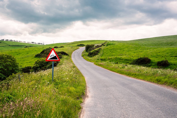 Señal de tráfico de advertencia de estilo europeo a lo largo de una carretera desierta empinada y sinuosa en un día nublado de primavera
 - Foto, imagen
