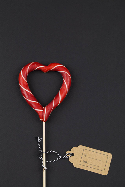 corazón rojo como caramelo de piruleta sobre fondo negro. Día de San Valentín fondo minimalista
. - Foto, Imagen
