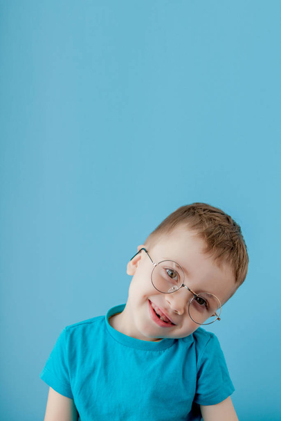 Portrait of a little smiling boy in a funny glasses. School. Preschool. Fashion. Studio portrait on a blue background, copy space - Foto, imagen