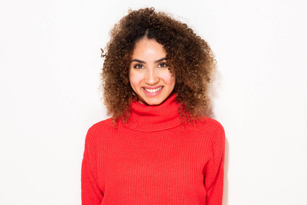 Primer retrato de una joven afroamericana sonriente con pelo rizado y suéter rojo por fondo blanco
 - Foto, Imagen