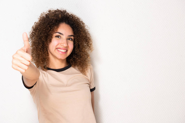 Portrait jeune femme heureuse avec les pouces vers le haut signe de la main par fond blanc
 - Photo, image