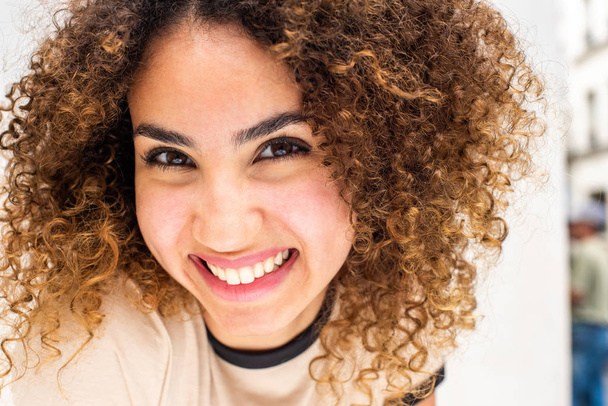 Close up portrait of beautiful young african american woman with curly hair smiling against white wall - Photo, Image