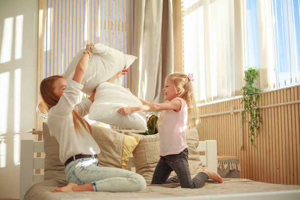 Μητέρα και κόρη παίζουν χαρούμενα μαζί με μαξιλάρια στο σπίτι  - Φωτογραφία, εικόνα