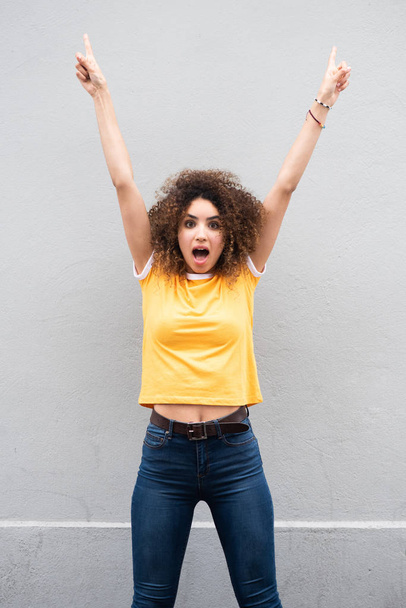 Portrait of cheerful young woman with arms raised and pointing fingers up - Photo, Image