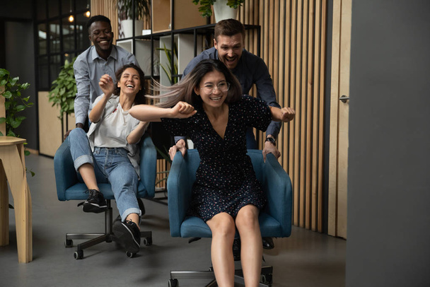 Overjoyed multiethnic colleagues have fun racing in office - Foto, Imagem