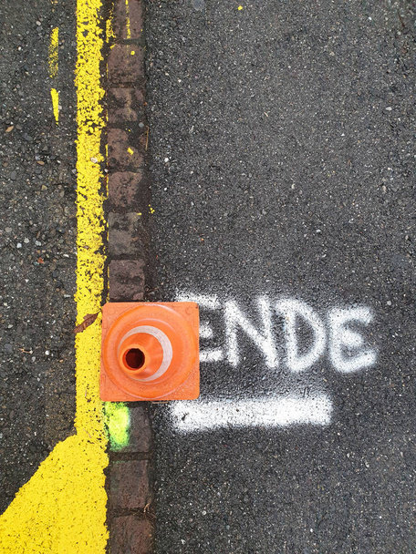 Cono de tráfico junto a la frontera de la carretera en la palabra alemana Ende escrito en blanco y subrayado
. - Foto, Imagen