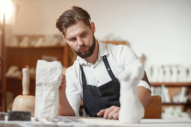 Bearded sculptor measures stone woman torso to make copy of it from limestone at creative studio. - Foto, afbeelding