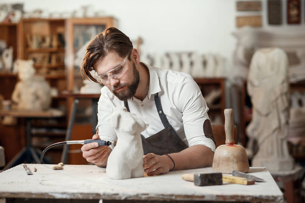 Male sculptor repairing gypsum sculpture of womans head at the working place in the creative artistic studio. - Фото, зображення