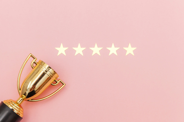 Simply flat lay design winner or champion gold trophy cup and 5 stars rating isolated on pink pastel background. Victory first place of competition. Winning or success concept. Top view copy space. - Photo, Image
