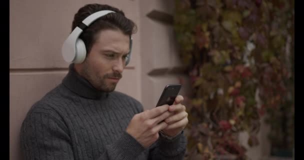 Happy man with phone in hands. Listen music on the headphone, and using phone - Záběry, video