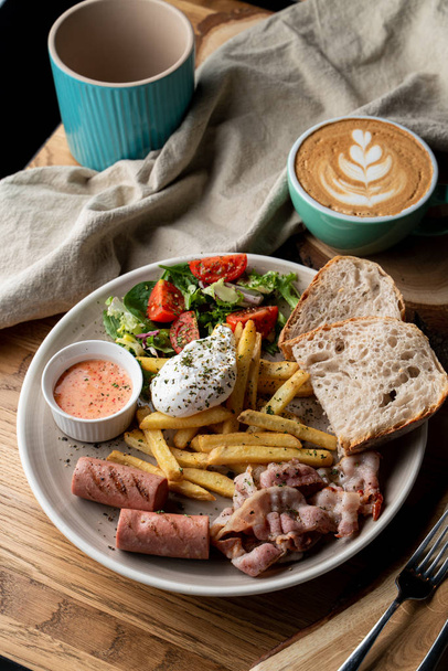 Substantieel ontbijt in een café met spek, geroosterde worst gepocheerd ei en salade - Foto, afbeelding