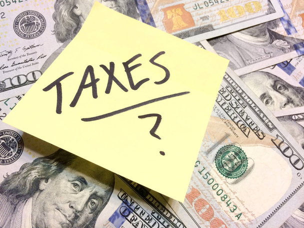 Dinero en efectivo estadounidense y amarilla nota con texto Impuestos con signo de interrogación
 - Foto, imagen