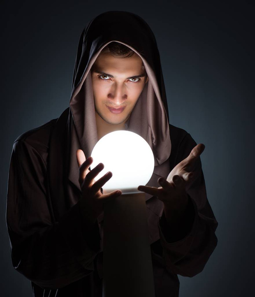 Jonge tovenaar met kristallen bol in donkere kamer - Foto, afbeelding