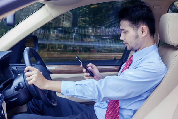 Businessman looking his mobile phone inside the car - Zdjęcie, obraz
