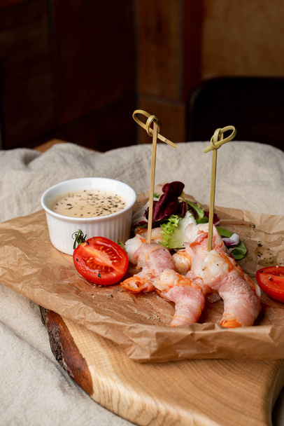 Close up of roasted shrimps wrapped in bacon with sauce and green salad - Photo, Image