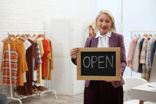 Female business owner holding OPEN sign in boutique. Space for text - Foto, afbeelding