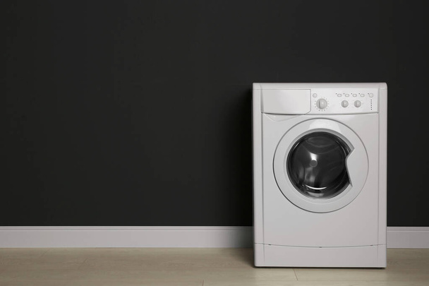 Modern washing machine near black wall, space for text. Laundry  - Photo, Image